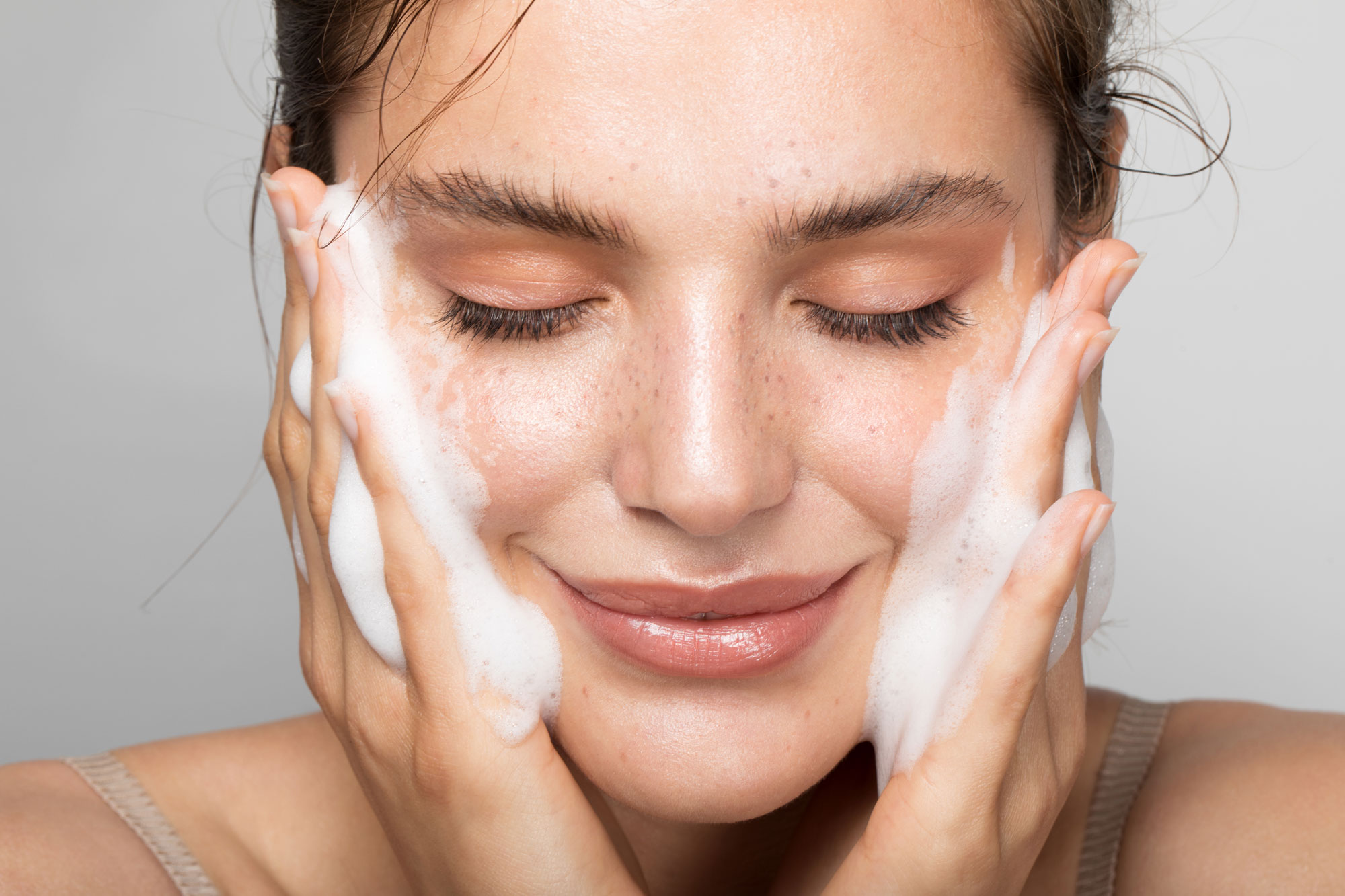 En kvinna ler och tvättar sitt ansikte med en produkt. Henne hy skiner.